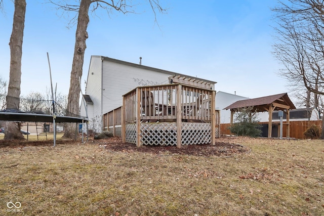 rear view of property featuring a trampoline, fence, and a wooden deck