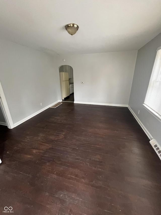 empty room featuring visible vents, baseboards, arched walkways, and dark wood-style flooring