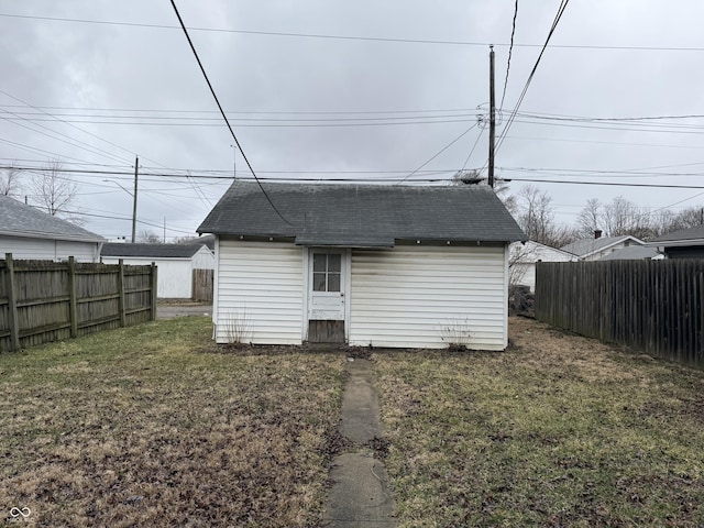 rear view of property featuring a lawn, roof with shingles, an outdoor structure, and fence