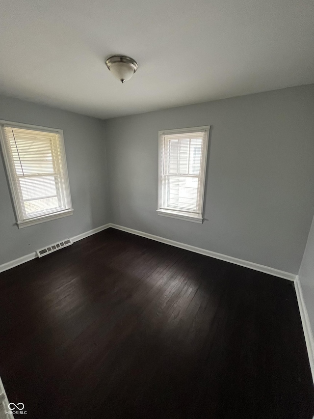 empty room featuring visible vents, baseboards, and dark wood finished floors