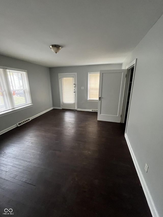 spare room featuring visible vents, dark wood-type flooring, and baseboards