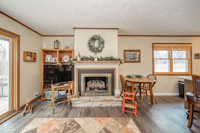 living area with ornamental molding, a fireplace with raised hearth, baseboards, and wood finished floors