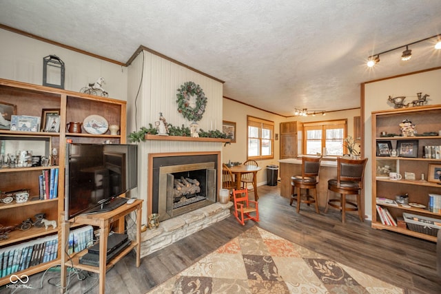 living area with a textured ceiling, a fireplace with raised hearth, wood finished floors, and crown molding