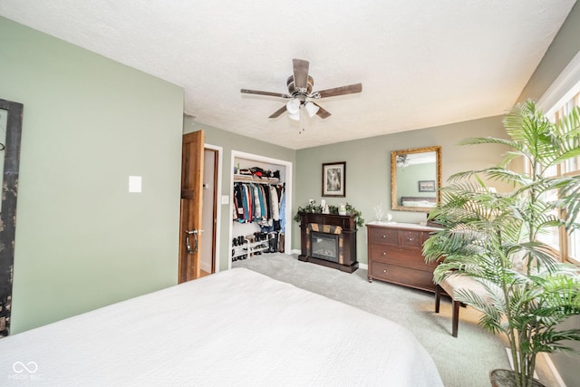 carpeted bedroom featuring a glass covered fireplace, a closet, ceiling fan, and a textured ceiling