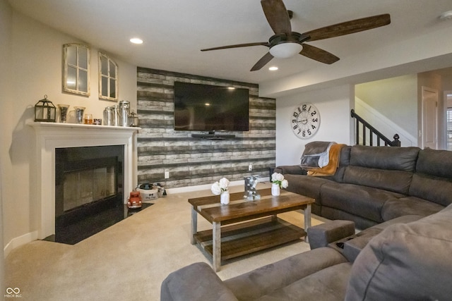 living area with wooden walls, recessed lighting, a fireplace with flush hearth, stairs, and carpet