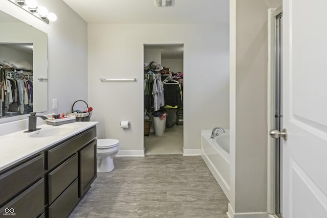 bathroom featuring toilet, vanity, wood finished floors, baseboards, and a bath