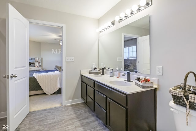 ensuite bathroom featuring double vanity, baseboards, ensuite bath, wood finished floors, and a sink