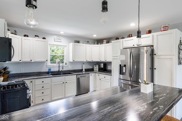 kitchen with stainless steel appliances, dark countertops, a sink, and white cabinetry