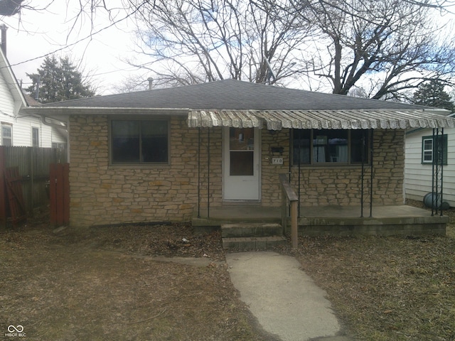 view of front of house featuring stone siding, fence, and roof with shingles