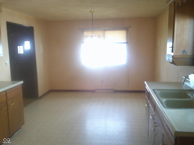 kitchen with light countertops, a sink, decorative light fixtures, and baseboards