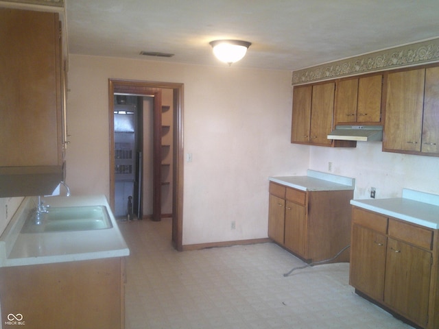 kitchen featuring under cabinet range hood, visible vents, brown cabinets, and light floors