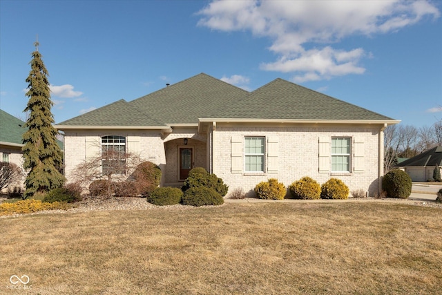 view of front of property with brick siding, a front lawn, and roof with shingles