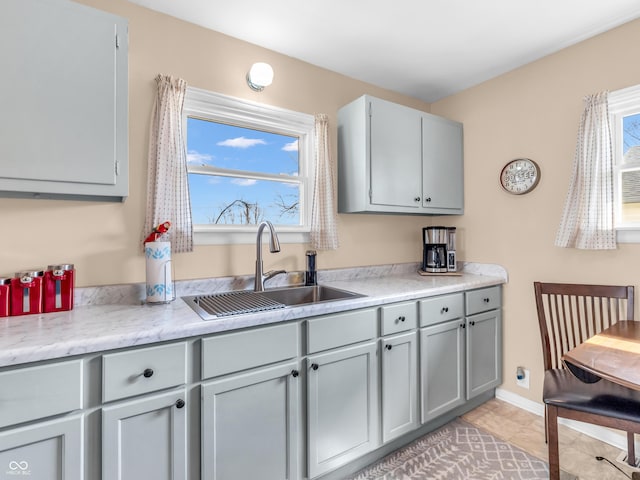 kitchen with gray cabinets, light countertops, a sink, and baseboards