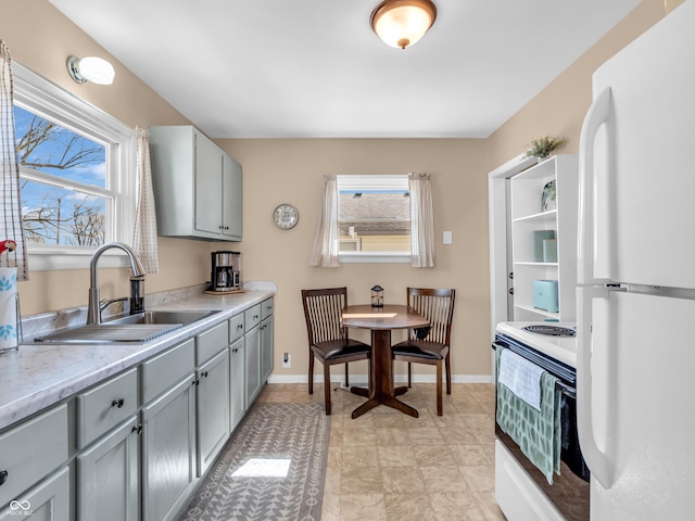 kitchen featuring gray cabinets, white appliances, a sink, and baseboards