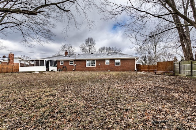 back of property with a sunroom, a fenced backyard, brick siding, and a chimney