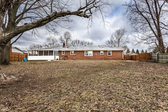 back of property with a sunroom, a fenced backyard, a chimney, and brick siding