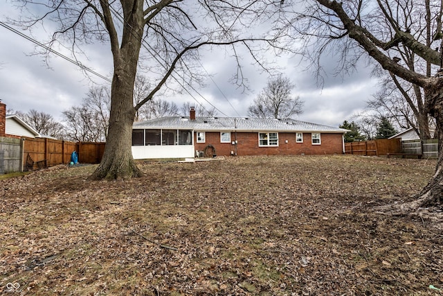 rear view of property featuring brick siding, a chimney, a fenced backyard, and a sunroom