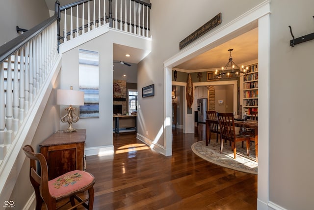 entryway featuring ornamental molding, wood finished floors, a towering ceiling, baseboards, and a chandelier