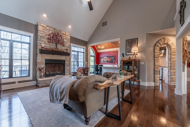 living area featuring a stone fireplace, dark wood-type flooring, and visible vents