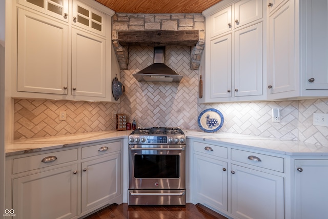 kitchen with backsplash, glass insert cabinets, wall chimney range hood, stainless steel gas stove, and dark wood-style flooring