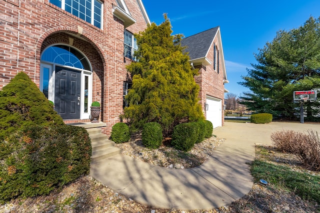 view of exterior entry featuring brick siding, roof with shingles, and concrete driveway