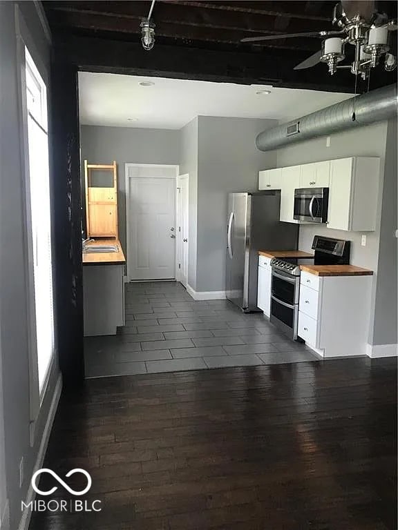 kitchen featuring dark wood-style floors, appliances with stainless steel finishes, white cabinets, wood counters, and baseboards