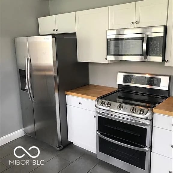 kitchen with baseboards, white cabinetry, stainless steel appliances, and dark tile patterned flooring