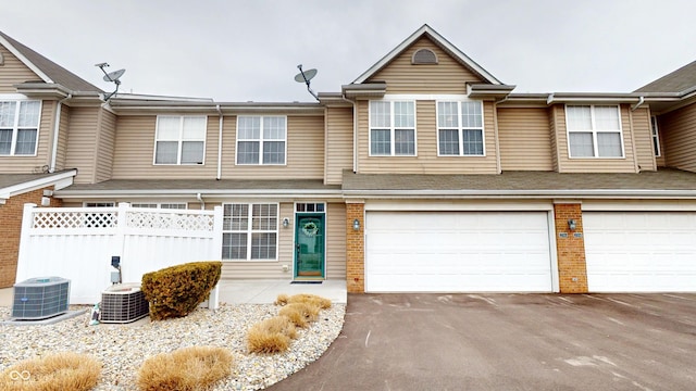 multi unit property featuring a garage, aphalt driveway, central AC unit, and fence