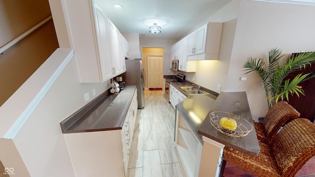 kitchen with a sink, dark countertops, white cabinetry, light wood-style floors, and appliances with stainless steel finishes