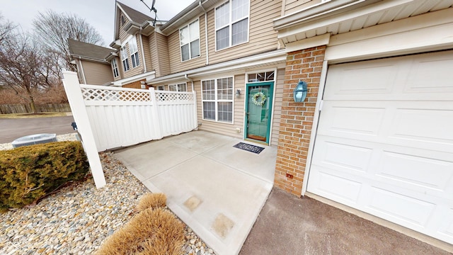 doorway to property featuring a garage, brick siding, and fence