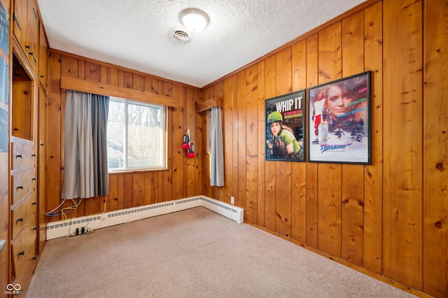 carpeted empty room featuring visible vents, wood walls, a textured ceiling, and a baseboard heating unit