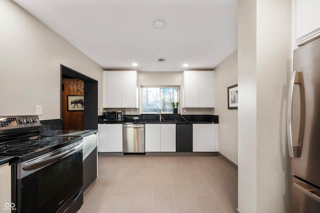 kitchen with dark countertops, white cabinets, appliances with stainless steel finishes, and a sink