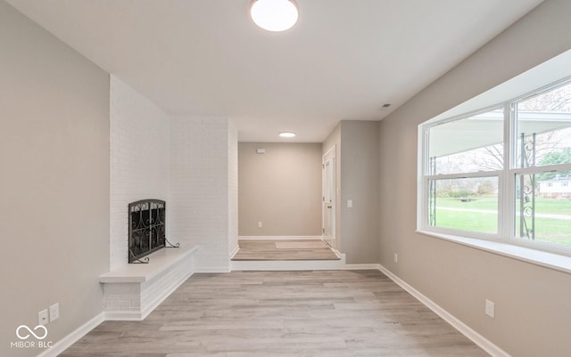 unfurnished living room with light wood finished floors, a brick fireplace, and baseboards