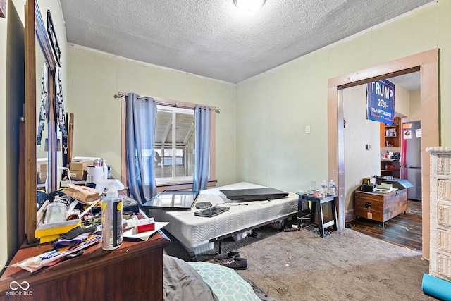 bedroom with a textured ceiling, carpet floors, and freestanding refrigerator