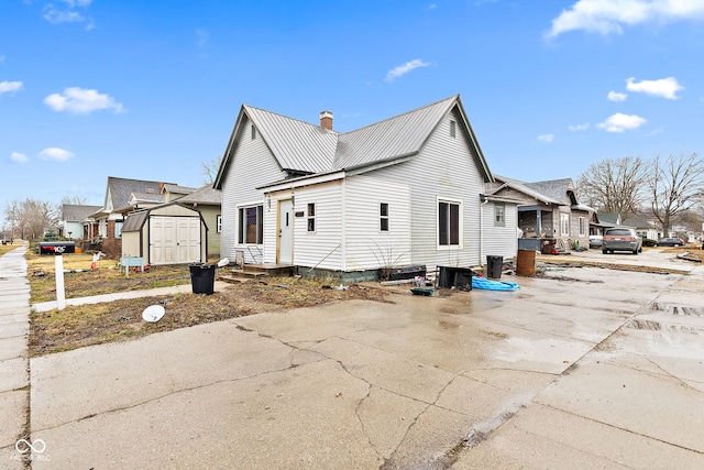 view of property exterior featuring a storage shed, a chimney, a residential view, metal roof, and an outbuilding