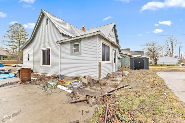 view of side of property with an outdoor structure, metal roof, a chimney, and a storage shed