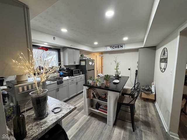 kitchen with light wood finished floors, appliances with stainless steel finishes, light stone counters, gray cabinetry, and recessed lighting