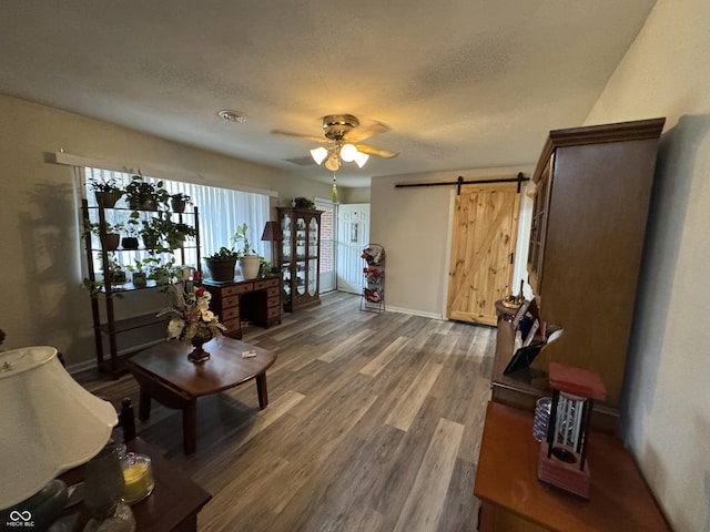 living area featuring a barn door, a ceiling fan, a textured ceiling, wood finished floors, and baseboards