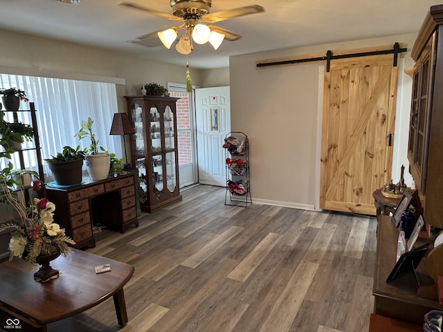 interior space featuring a barn door, baseboards, ceiling fan, and wood finished floors