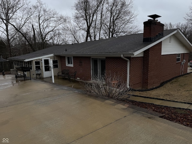 back of house featuring brick siding, a chimney, and a shingled roof