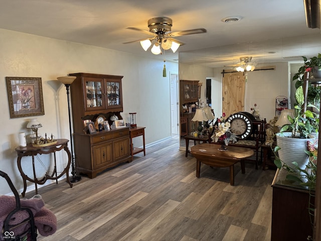 interior space featuring visible vents, a barn door, ceiling fan, wood finished floors, and baseboards