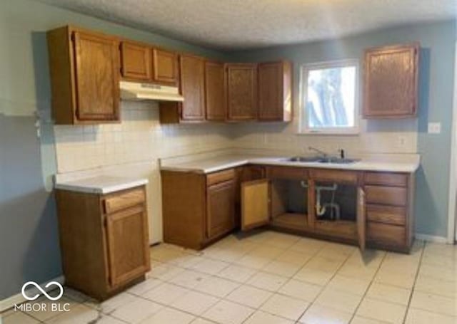 kitchen featuring brown cabinets, light countertops, a textured ceiling, under cabinet range hood, and backsplash