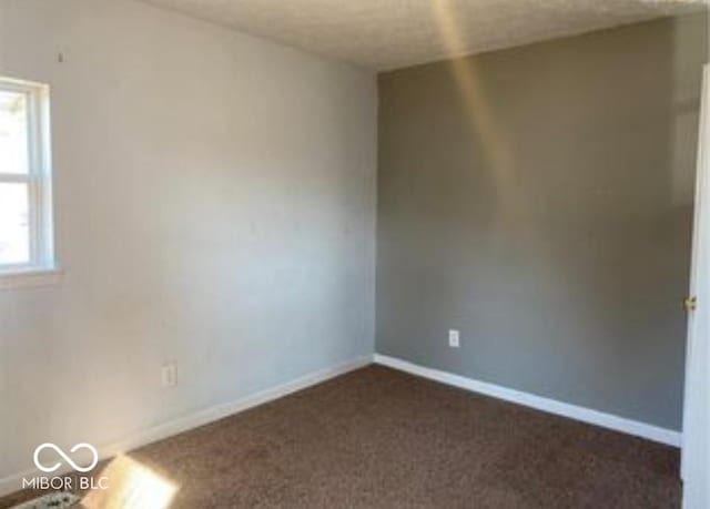 spare room featuring dark carpet and baseboards