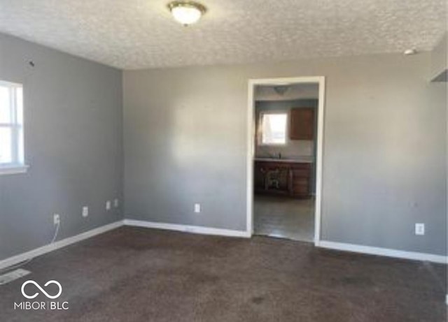 spare room with a textured ceiling, dark colored carpet, and baseboards