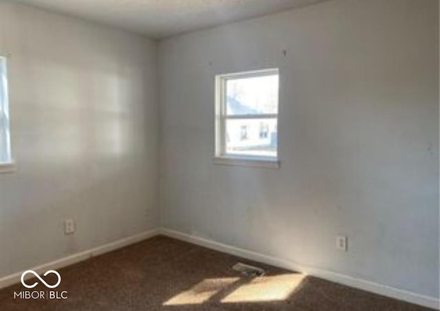 spare room featuring baseboards and dark carpet