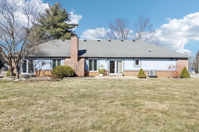 rear view of house featuring a yard, brick siding, roof with shingles, and a chimney