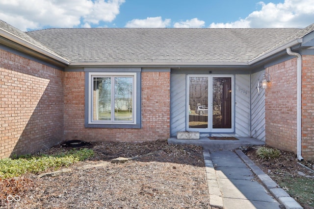 view of exterior entry featuring brick siding and roof with shingles