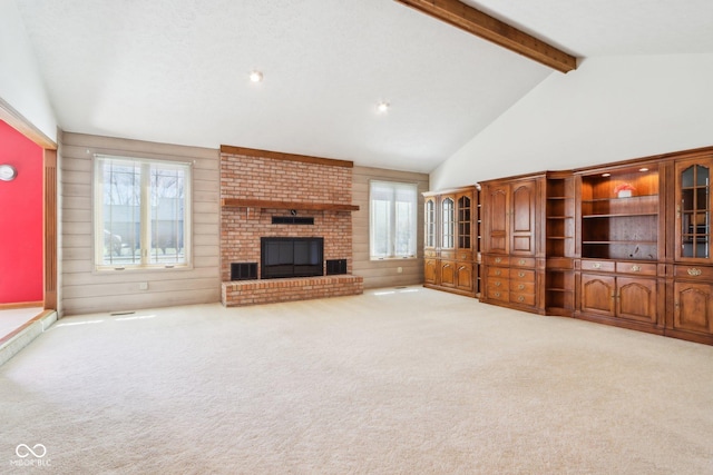 unfurnished living room featuring beam ceiling, high vaulted ceiling, carpet floors, wooden walls, and a fireplace