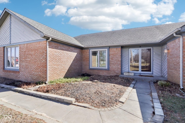 property entrance featuring brick siding and a shingled roof