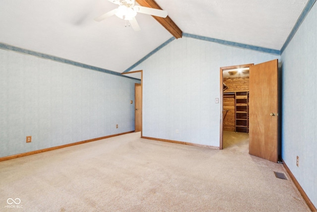 empty room featuring a ceiling fan, carpet, visible vents, baseboards, and lofted ceiling with beams